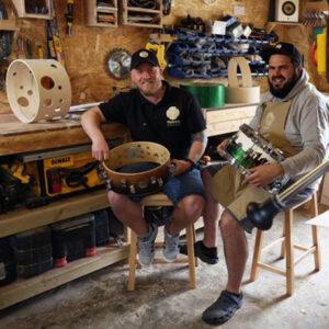 Two man sitting down holding drum parts in a drum studio